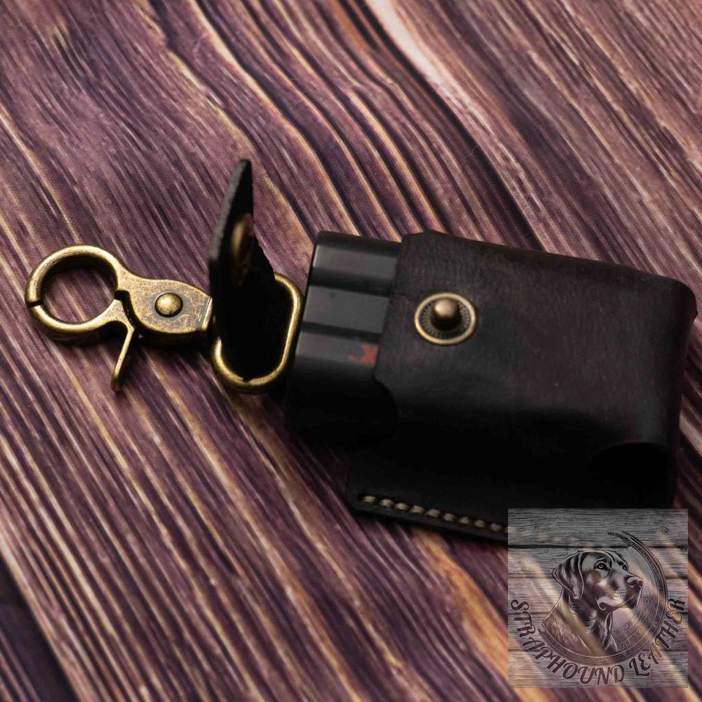 photo of wood grain background with a black leather camera batter pouch with antique brass hardware