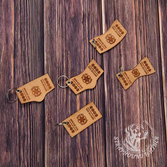 photo showing 5 service dog shaped and laser engraved keychains in natural leather with silver split rings depicting miniature replicas of service dog vests on a wood grain background