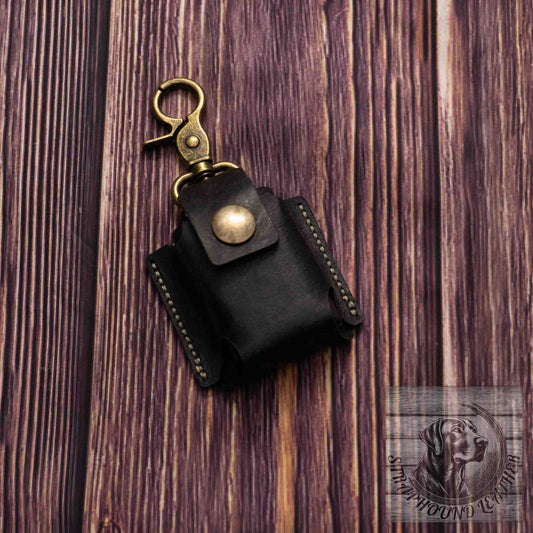 photo of wood grain background with a black leather camera batter pouch with antique brass hardware