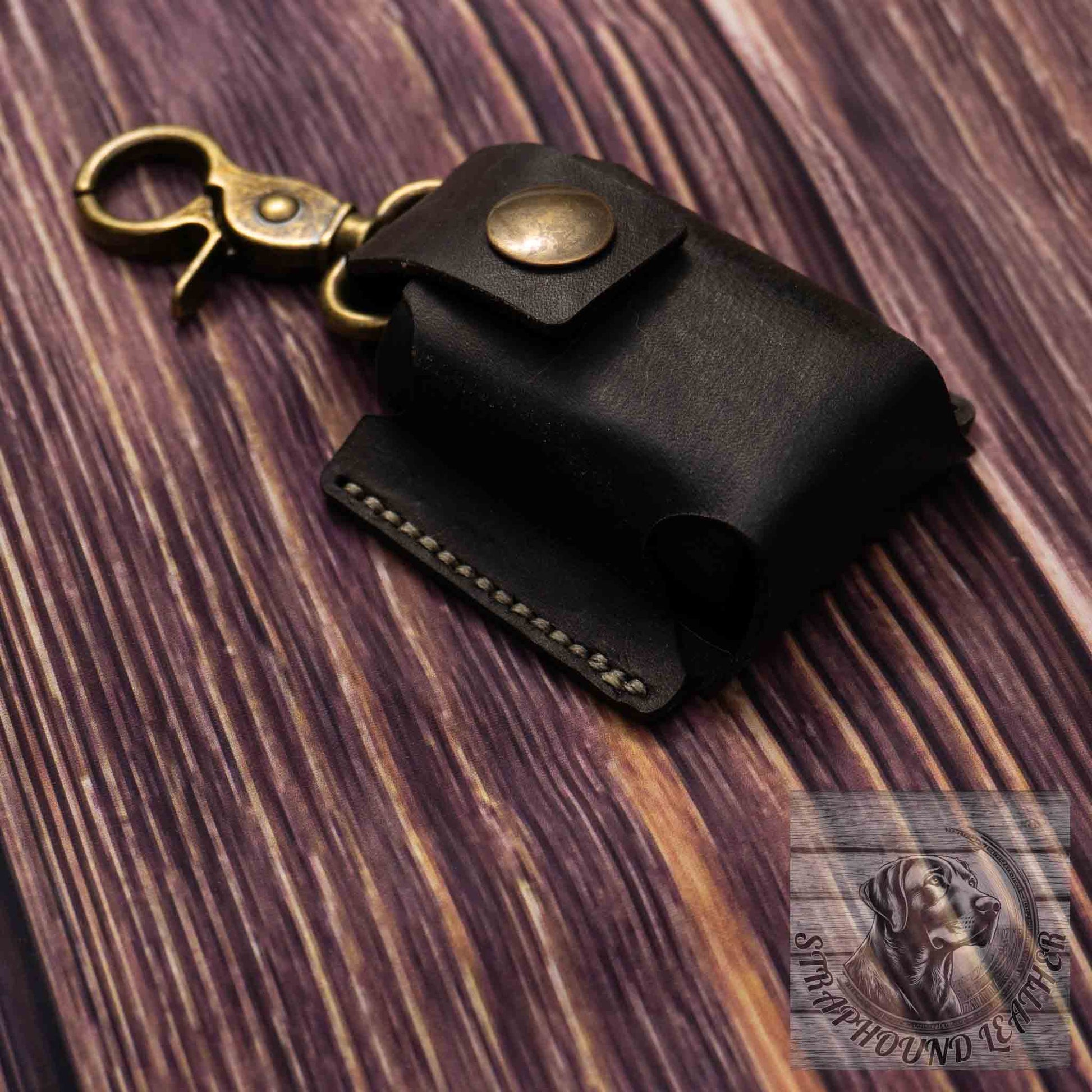 photo of wood grain background with a black leather camera batter pouch with antique brass hardware