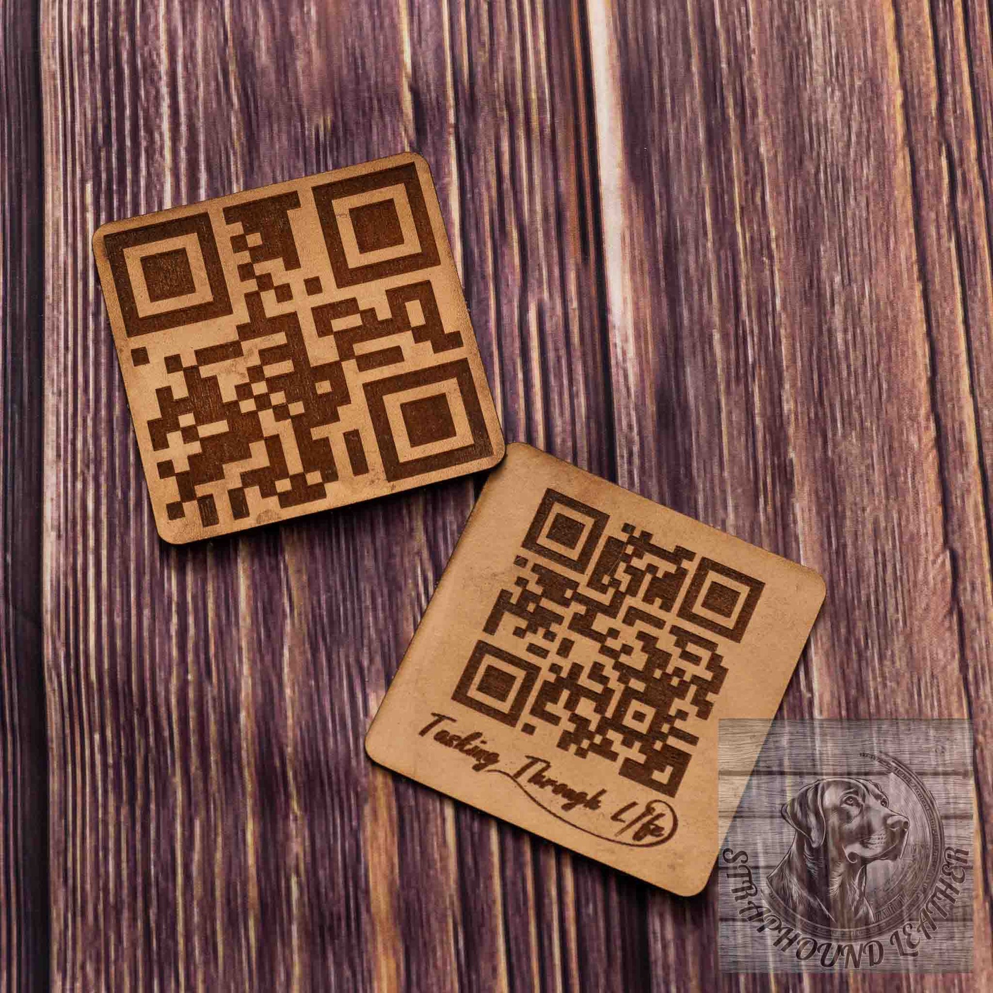 photo showing two coasters in a natural leather with a QR scan-able code laser engraved on them on a wood grain background. 