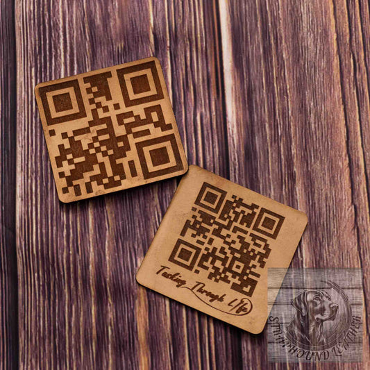 photo showing two coasters in a natural leather with a QR scan-able code laser engraved on them on a wood grain background. 